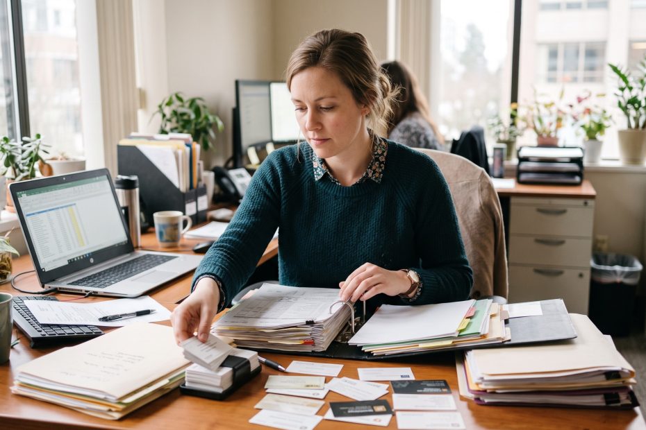Vendor consolidation: a purchasing coordinator sorting supplier folders and contractor business cards to trim a bloated vendor list